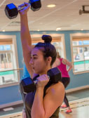 woman exercising with dumbbell over head in gym
